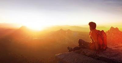 Man with backpack sitting down looking across mountains