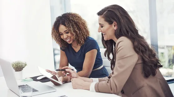 Two women looking at tablet with computer on table